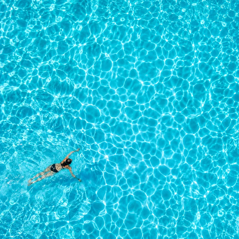 A swimmer in a turquoise pool filled with sunlight patterns